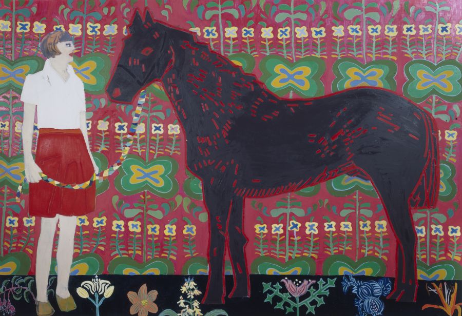 A woman holding a horse in front of a decorative wall.