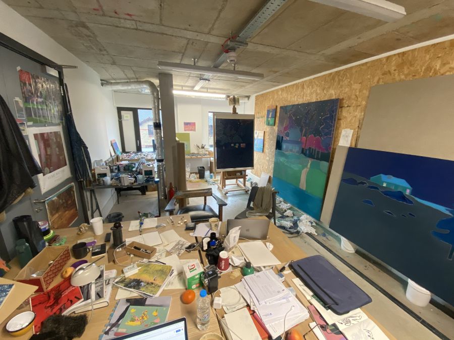 Photograph of an art studio with paintings, desks and papers.